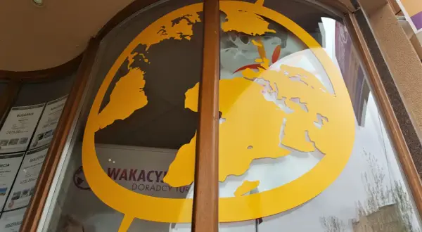 Żółta mapa świata na szybie biura podróży z widocznymi ofertami wakacyjnymi.